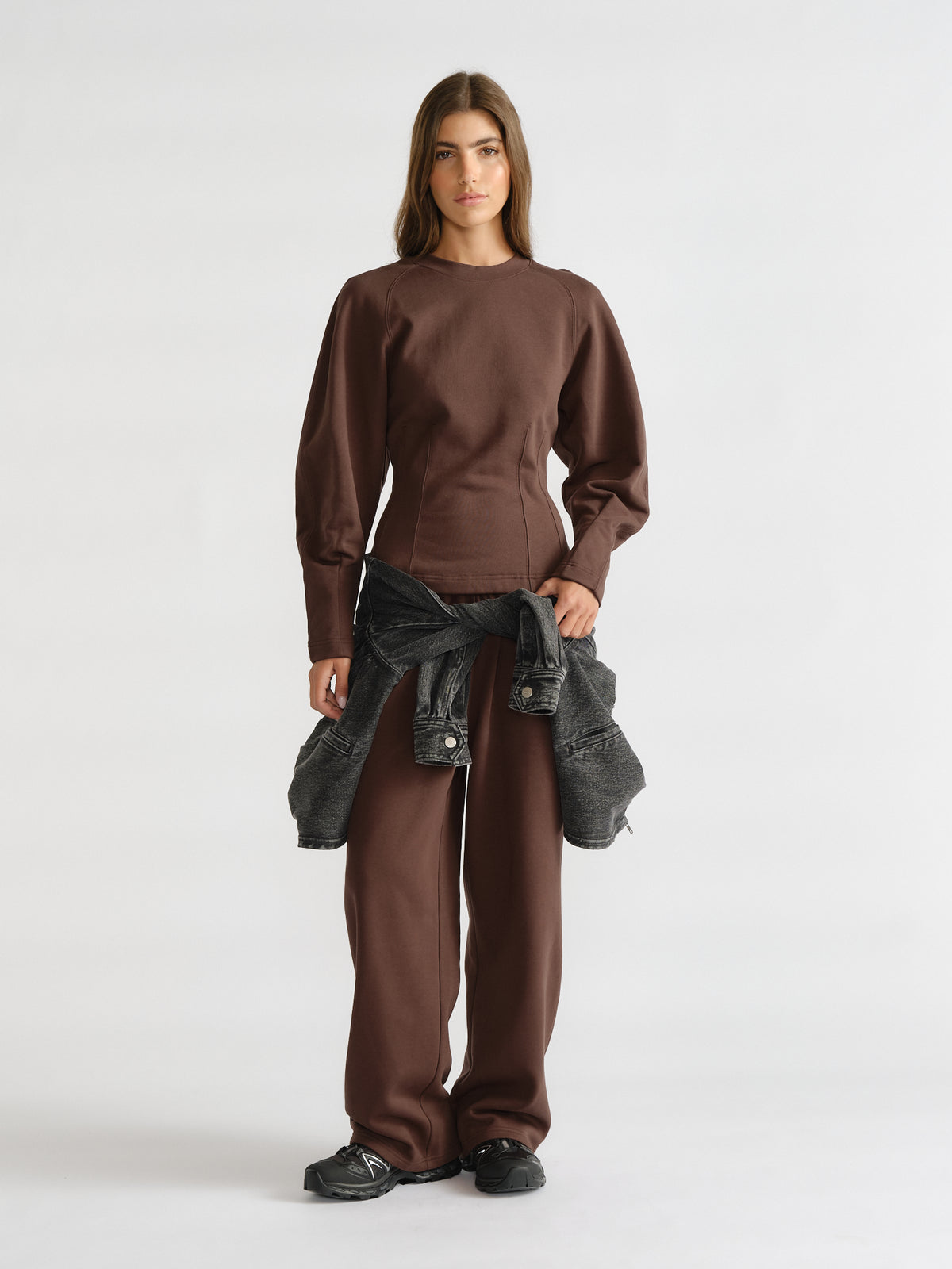 Woman wearing a rich brown cinched waist sweatshirt with relaxed matching pants and a black denim jacket tied at the waist