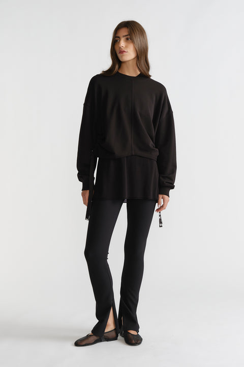 Woman wearing black D-Luxe Ruched Terry Sweat with relaxed fit and drawstring details, paired with slim black pants and flats