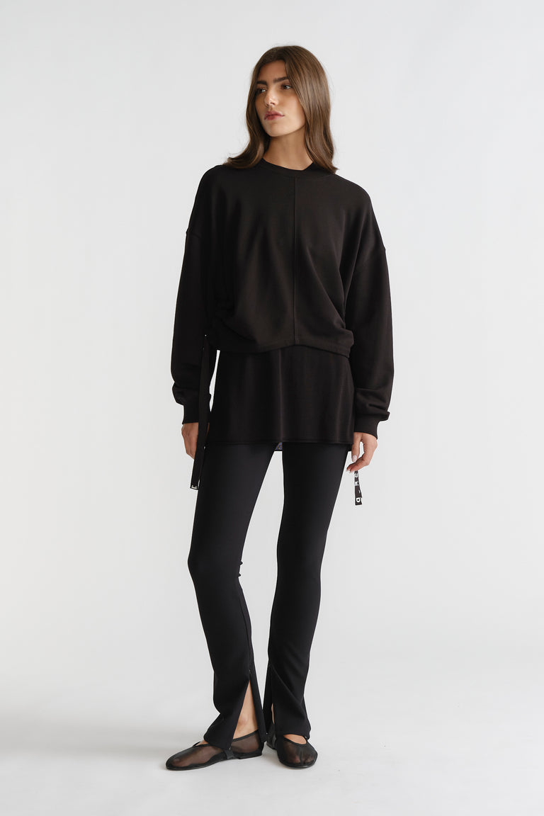 Woman wearing black D-Luxe Ruched Terry Sweat with relaxed fit and drawstring details, paired with slim black pants and flats