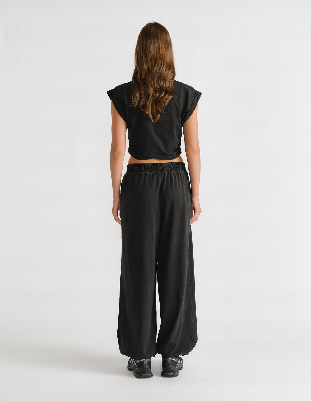 Model wearing a black cropped tank top with extended sleeves, viewed from behind
