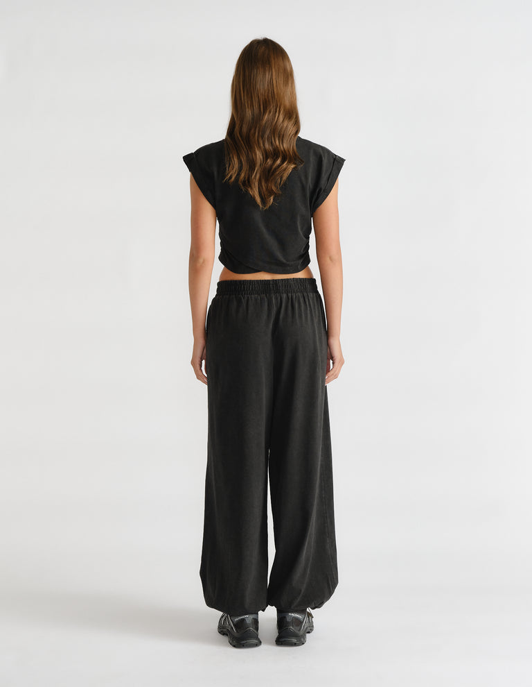 Model wearing a black cropped tank top with extended sleeves, viewed from behind