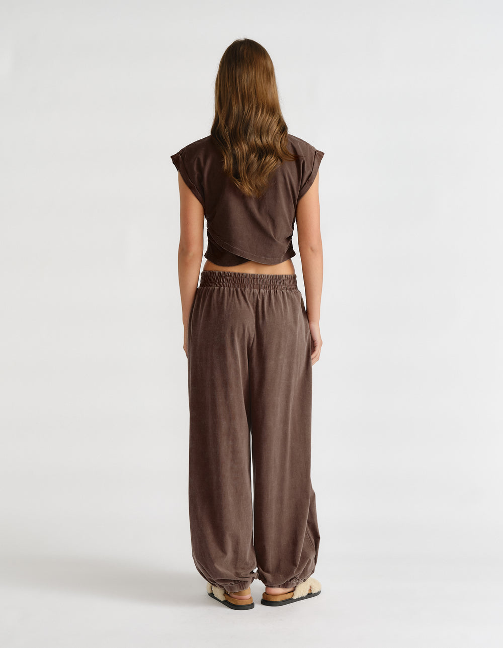 Back view of a woman wearing a brown cropped tank top with a crossover hem and relaxed wide-leg pants