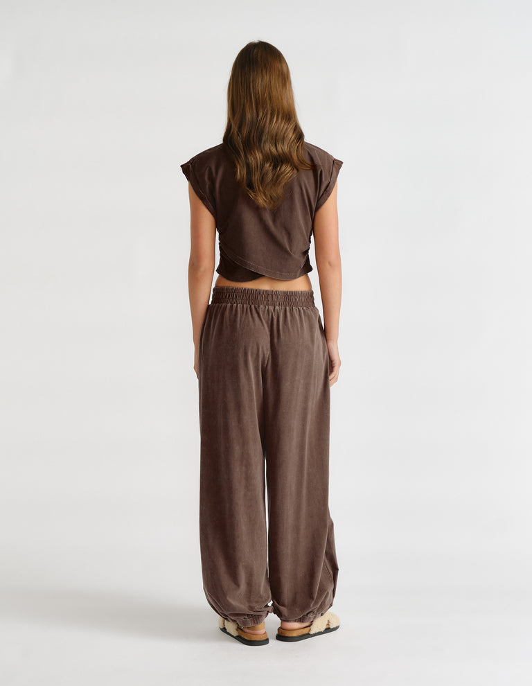 Back view of a woman wearing a brown cropped tank top with a crossover hem and relaxed wide-leg pants