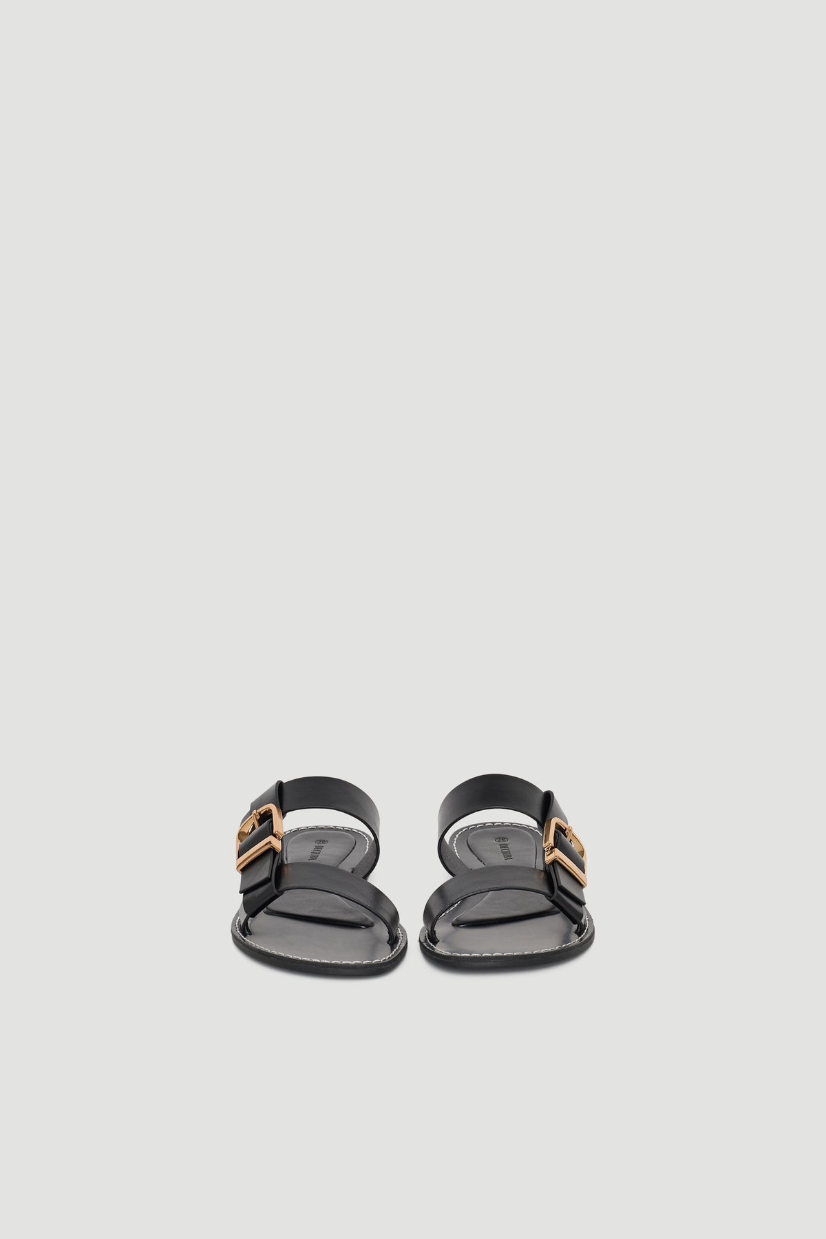 Black flat sandals with wide straps and gold buckle details for a sleek, minimalist summer look