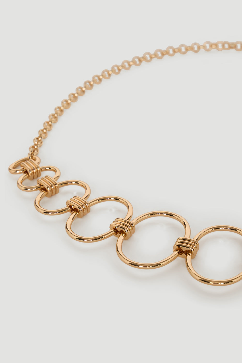 Close-up of a gold chain belt featuring linked circular loops with wrapped detail on a light background.