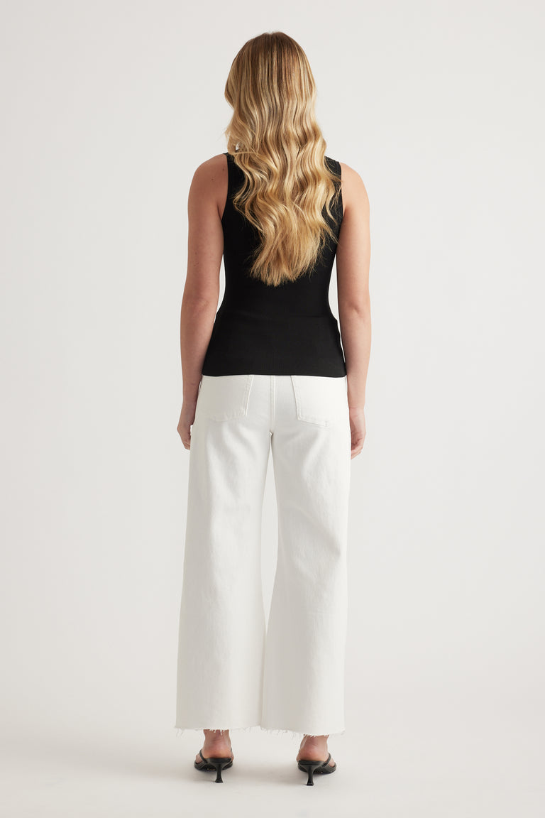 Woman wearing a fitted black sleeveless knit top with white wide-leg jeans and heels, viewed from behind