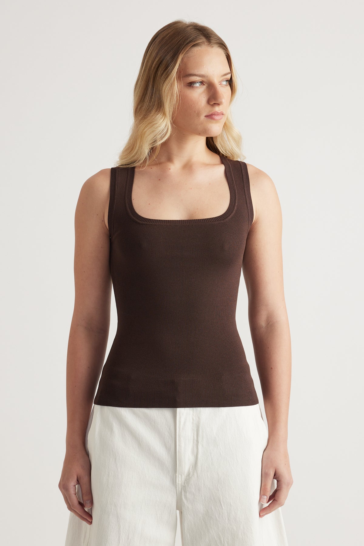 Woman wearing a fitted brown square-neck knit tank top with white pants