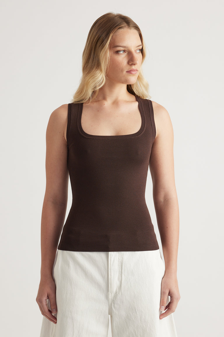 Woman wearing a fitted brown square-neck knit tank top with white pants
