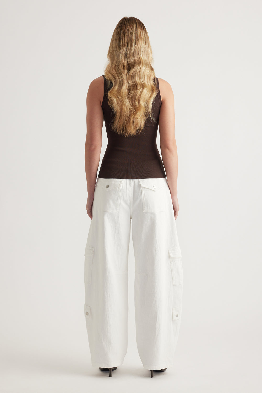 Woman wearing a fitted brown sleeveless tank with white cargo pants, viewed from behind