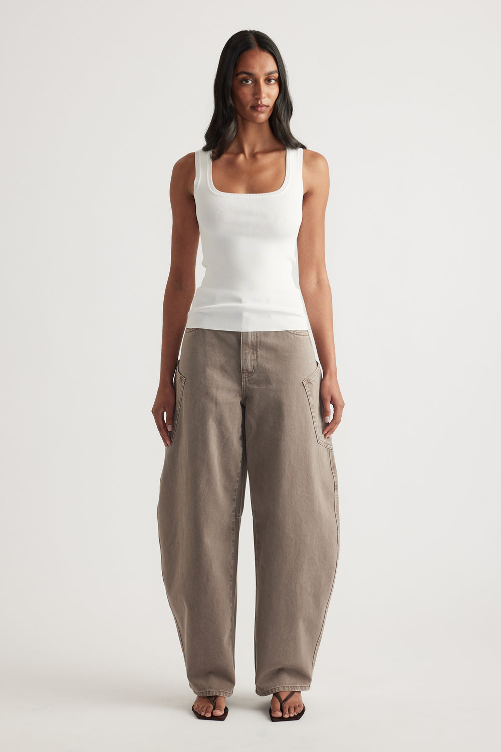 Woman wearing a white fitted square-neck tank top with taupe balloon-leg pants and sandals