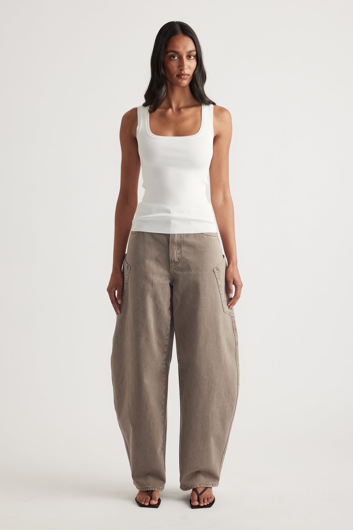 Woman wearing a white fitted square-neck tank top with taupe balloon-leg pants and sandals