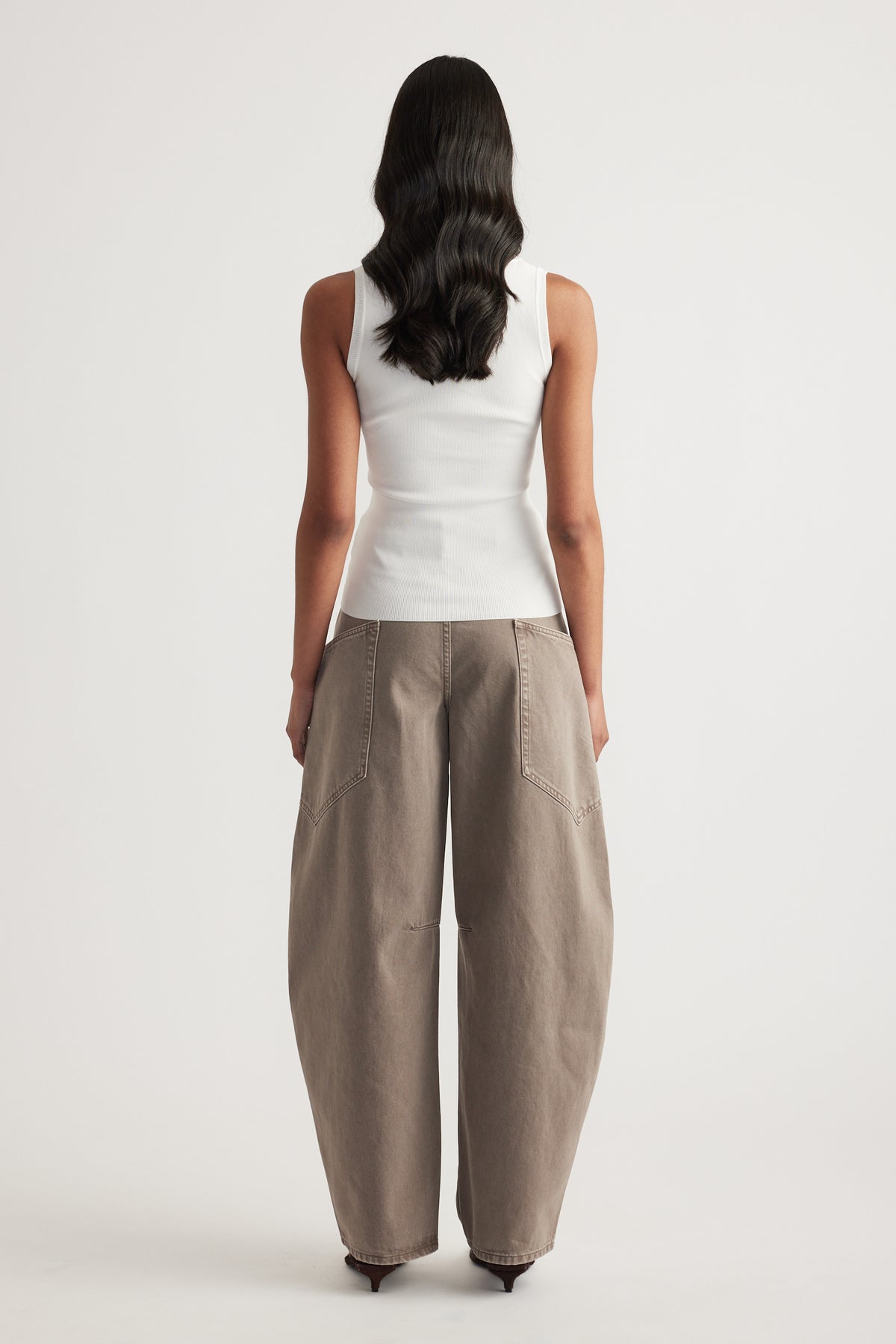 Back view of a woman wearing a fitted white sleeveless tank with taupe wide leg pants