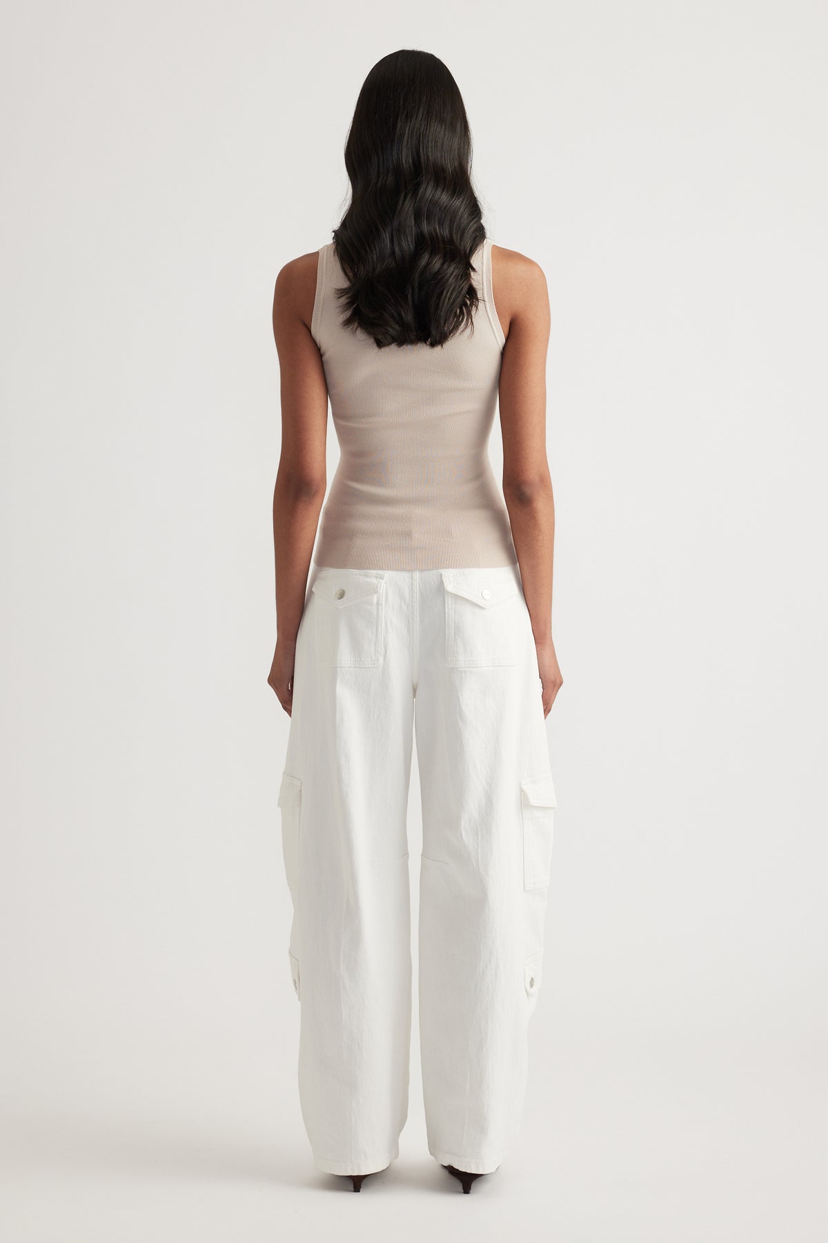 Woman viewed from behind wearing a beige fitted knit tank and white wide-leg cargo pants