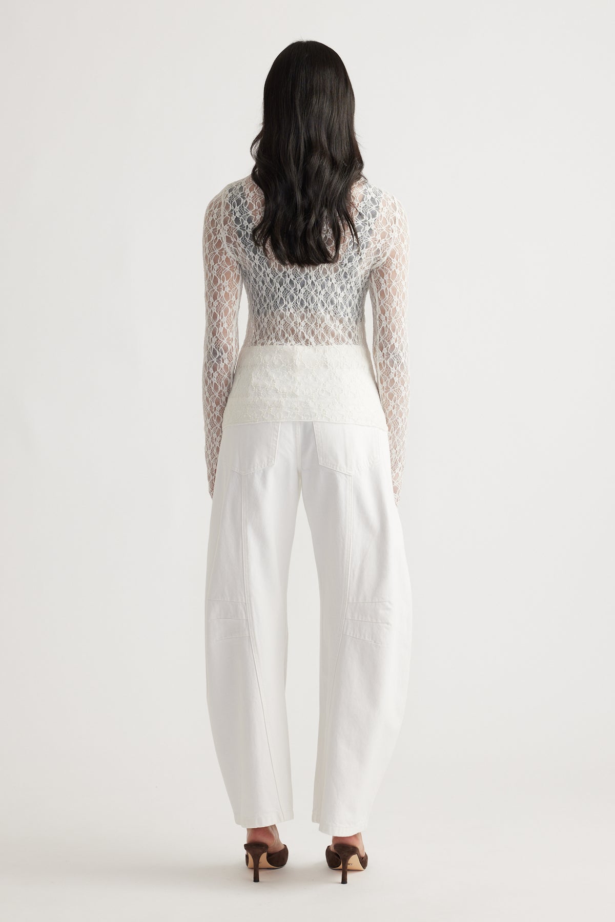 Back view of a delicate cream lace long sleeve top paired with wide-leg white denim jeans and brown heels