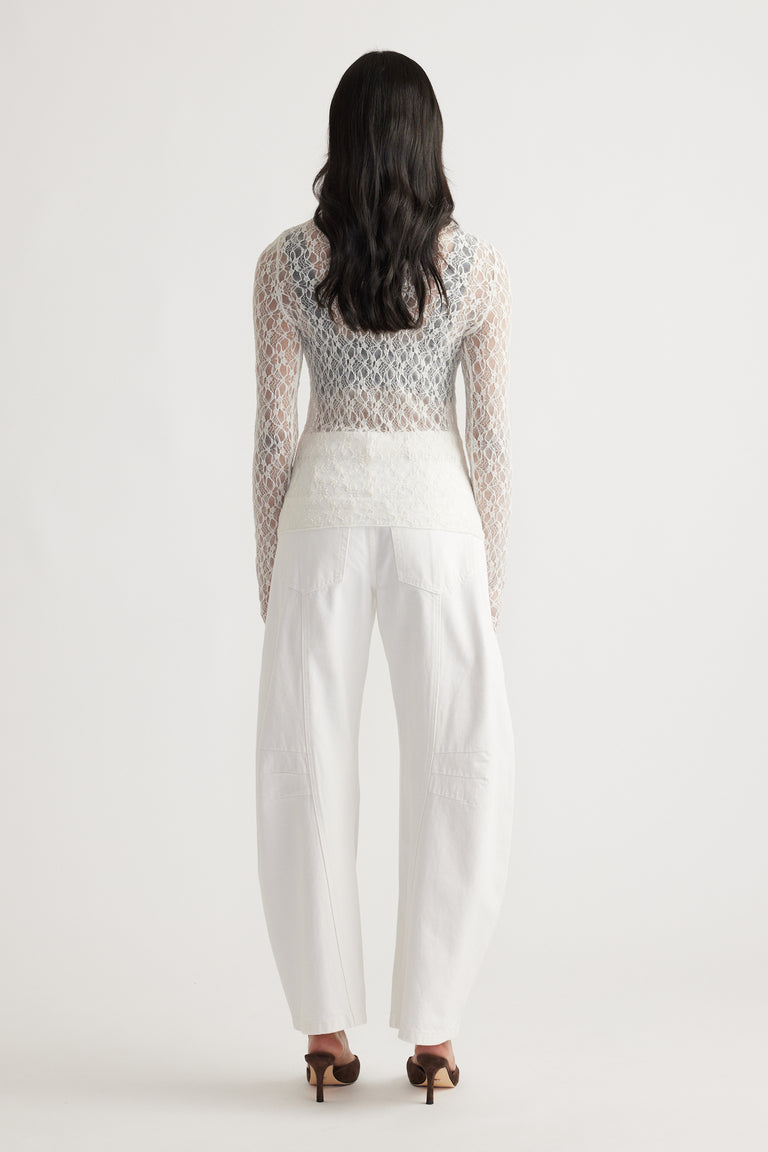 Back view of a delicate cream lace long sleeve top paired with wide-leg white denim jeans and brown heels