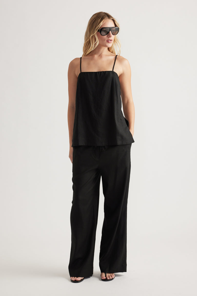 Woman wearing relaxed black linen blend pants paired with a sleeveless square-neck top and oversized sunglasses.