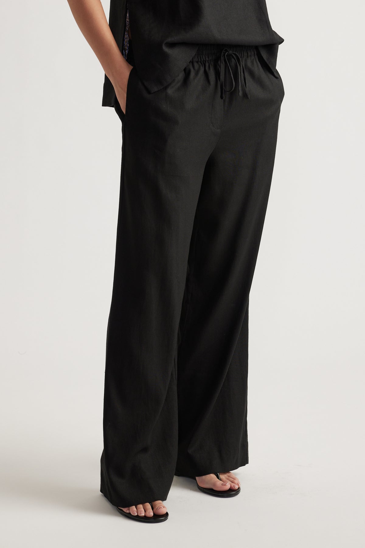 Relaxed fit black linen blend pants with wide legs and drawstring waist, styled casually with sandals and a loose top.