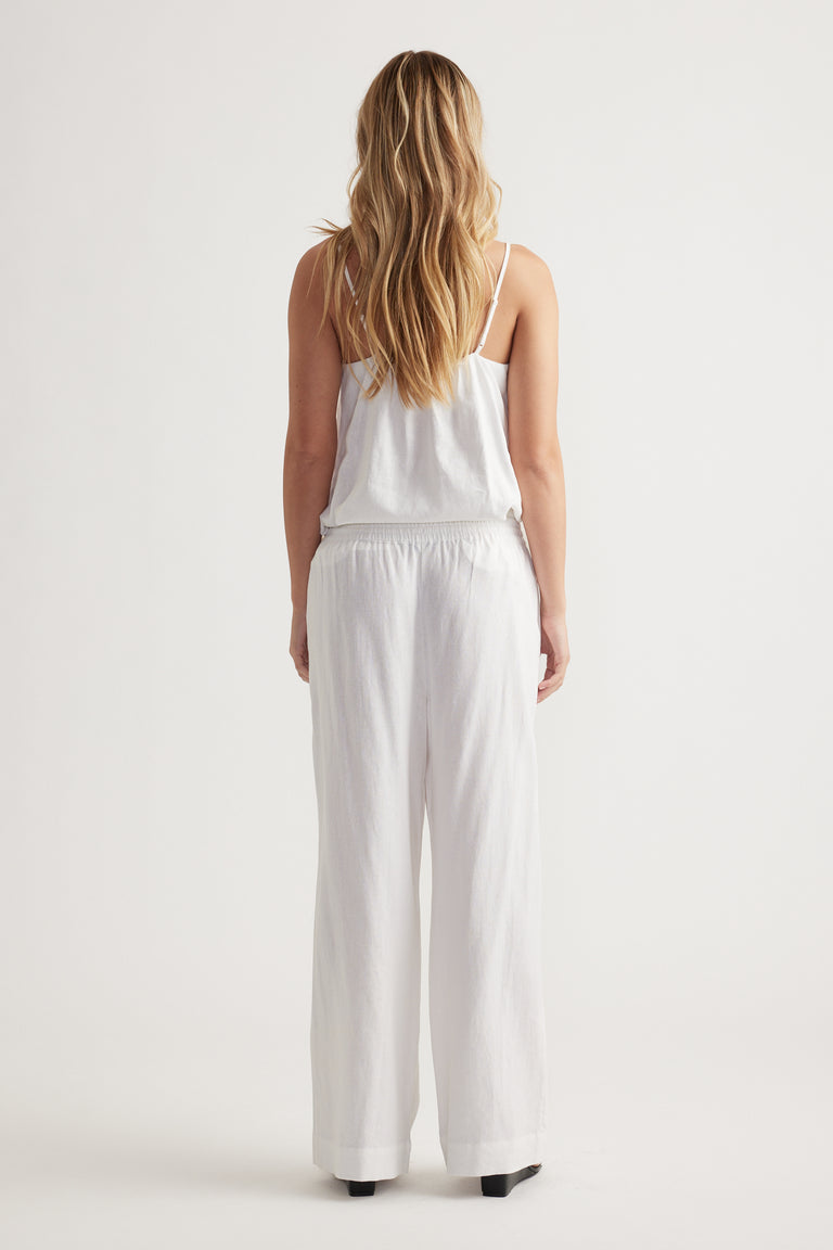 Woman wearing relaxed fit white linen blend pants with elastic waistband and a white sleeveless top, shown from behind