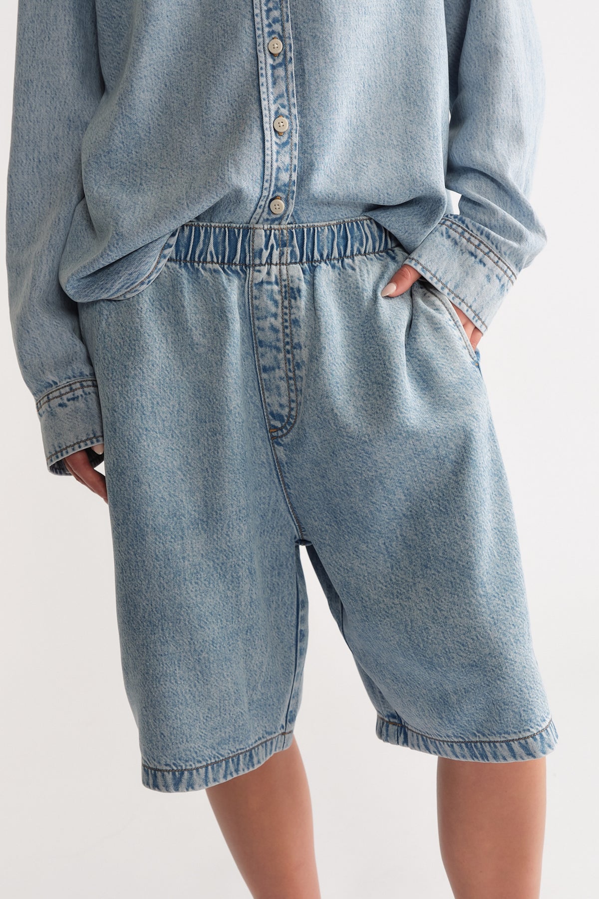 Woman wearing relaxed light blue denim shorts with elastic waist paired with a casual long-sleeve denim shirt