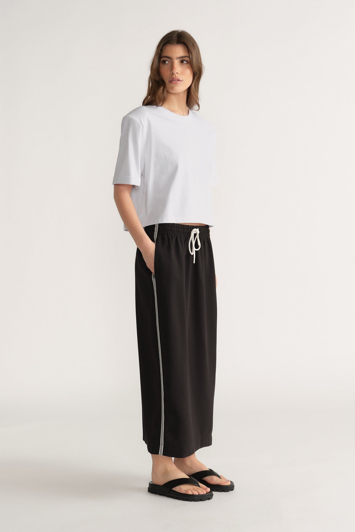 Woman wearing a black midi skirt with white racer stripes and drawcord waist, a white tee and black sandals