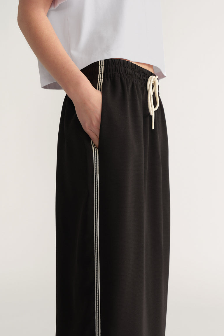 Woman wearing a black midi skirt with elastic waist and side stripe, paired with a white tee