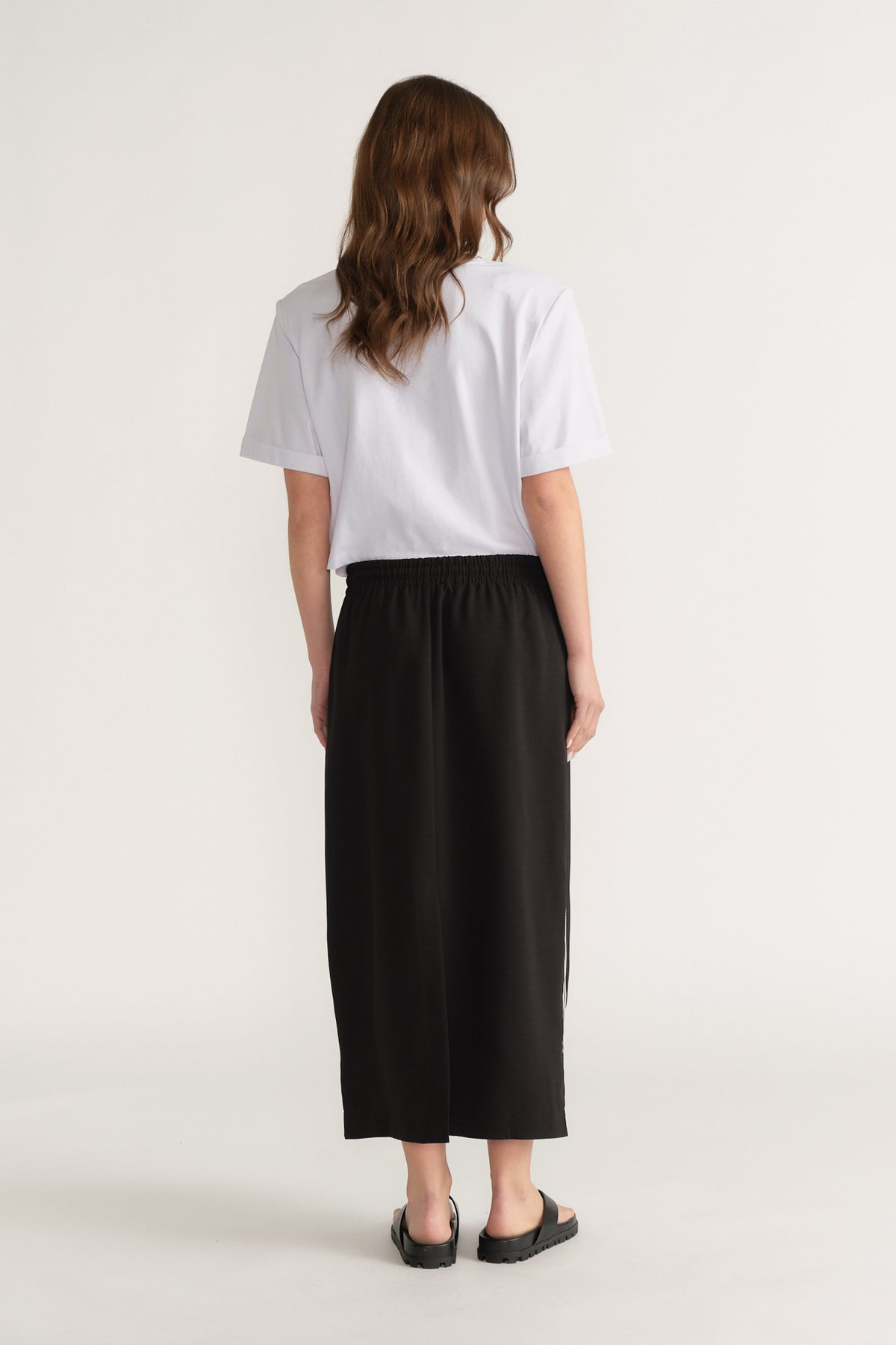 Woman wearing a white T-shirt with a black elastic waist midi skirt and black sandals