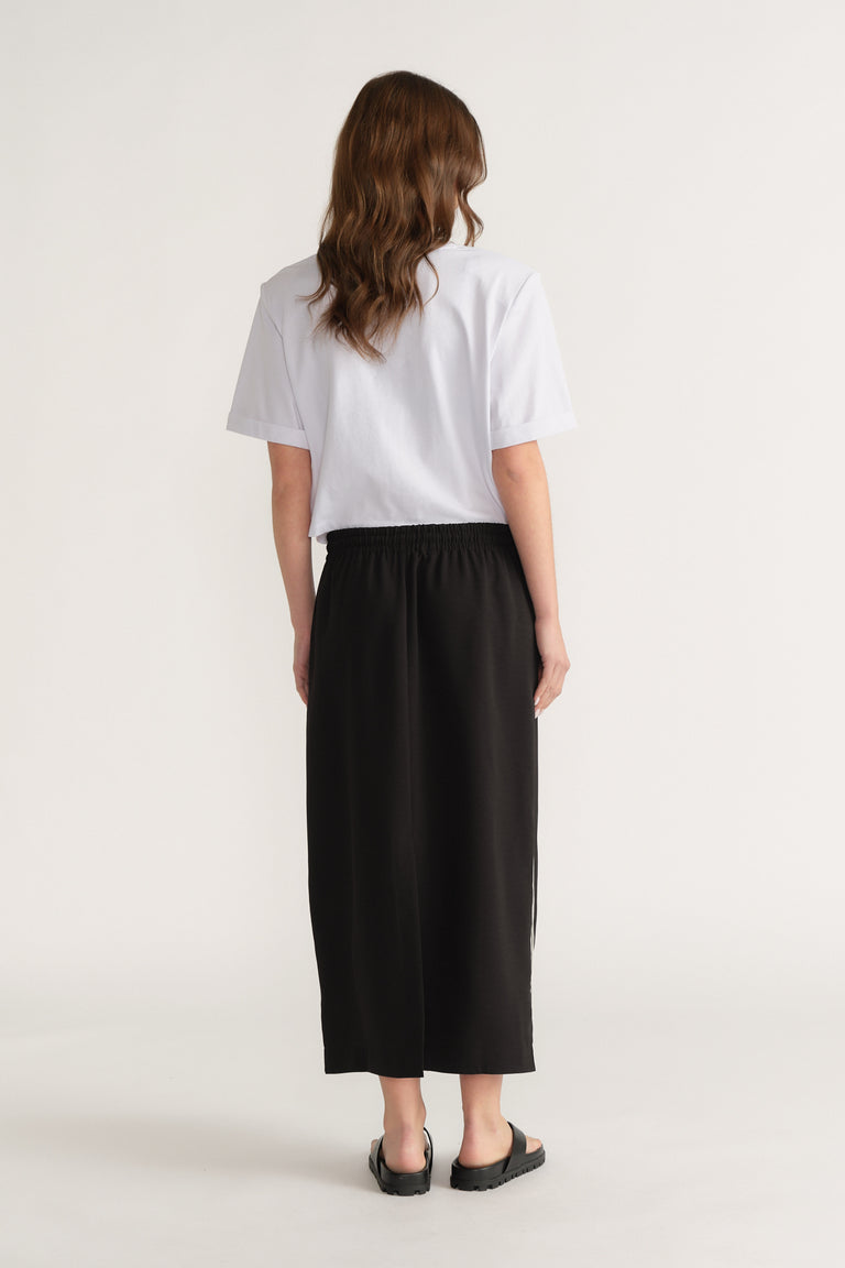 Woman wearing a white T-shirt with a black elastic waist midi skirt and black sandals