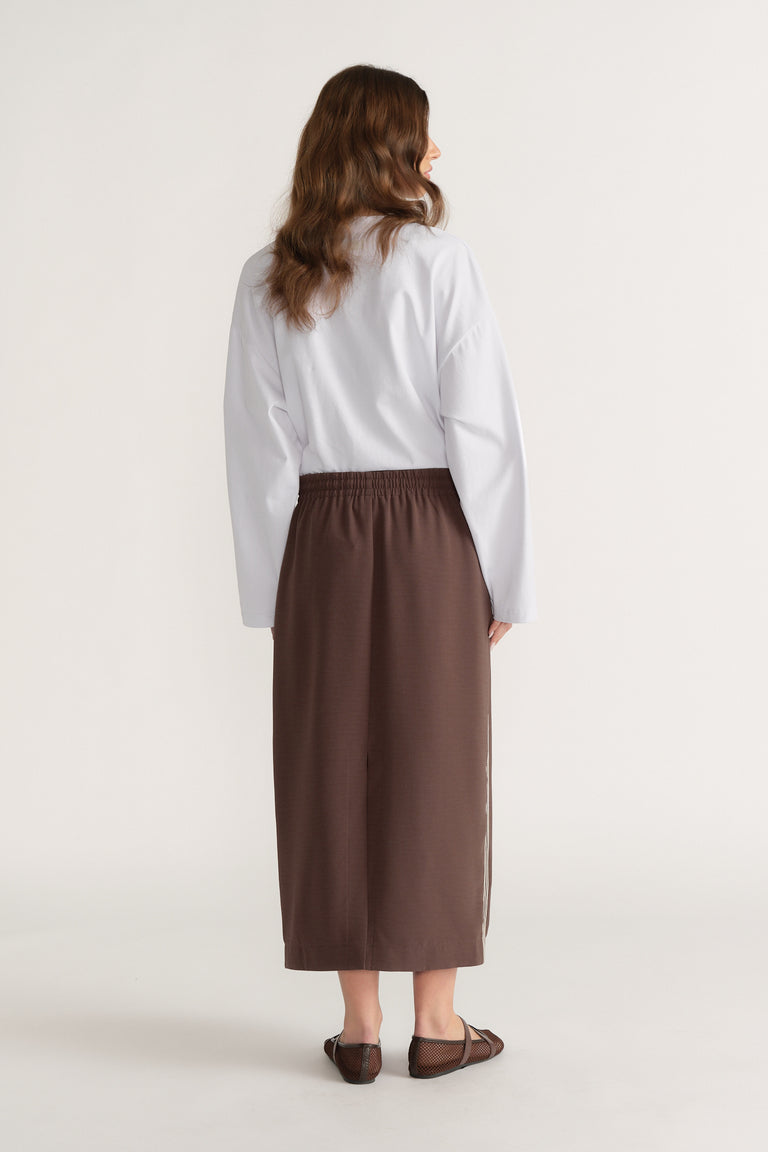 Woman wearing a brown midi skirt with side stripe, white shirt and flat sandals