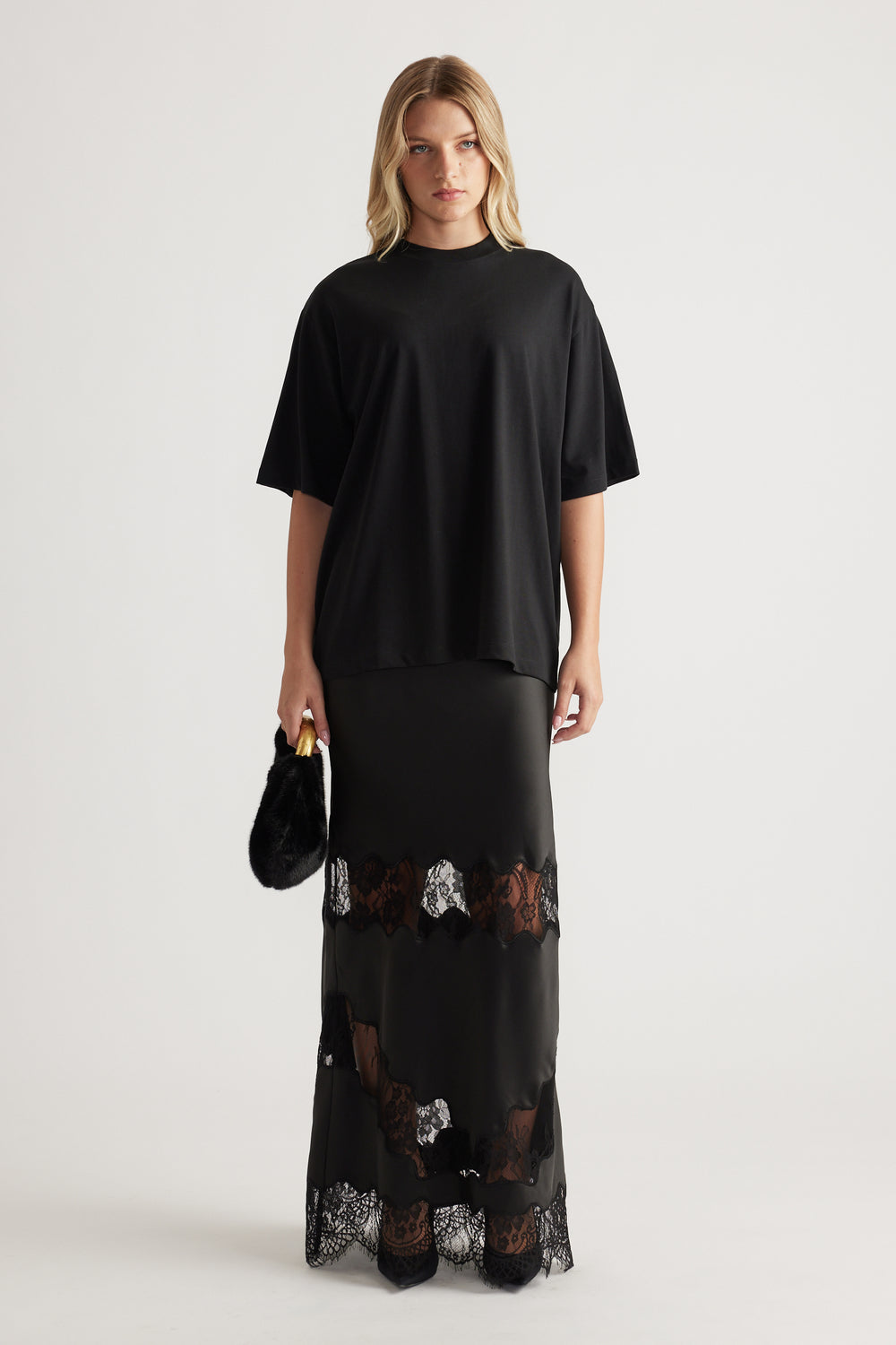 Woman wearing a loose black oversized tee paired with a long black skirt featuring lace panels and holding a small black bag
