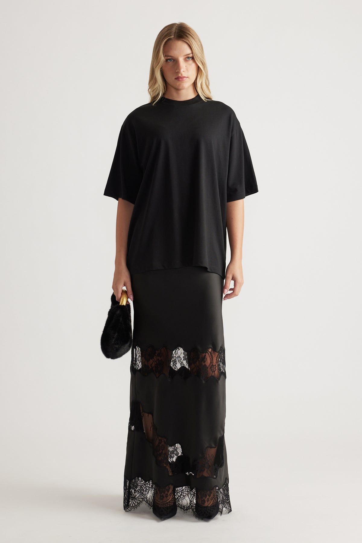 Woman wearing a loose black oversized tee paired with a long black skirt featuring lace panels and holding a small black bag