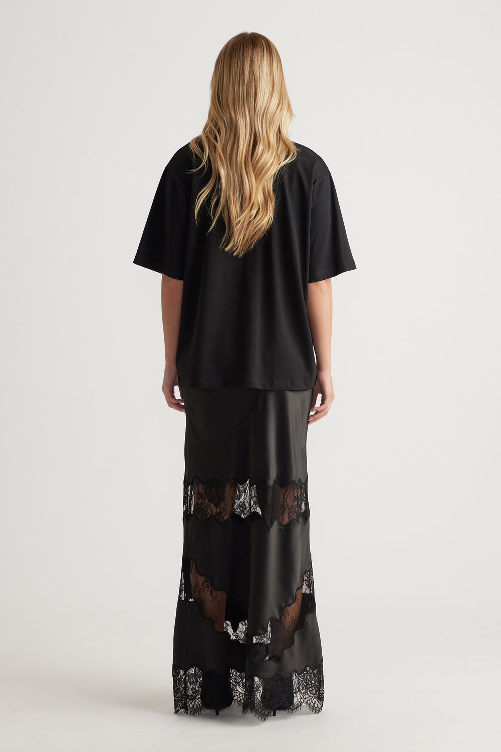 Back view of woman wearing a relaxed black oversized tee paired with a floor-length black lace-trimmed skirt