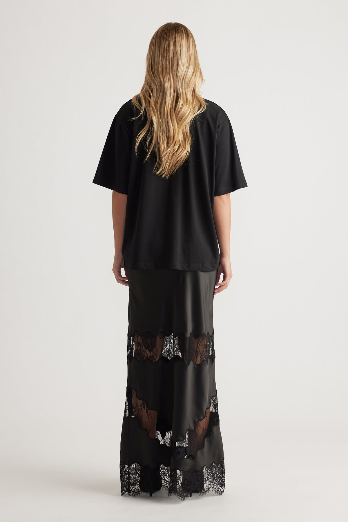 Back view of woman wearing a relaxed black oversized tee paired with a floor-length black lace-trimmed skirt