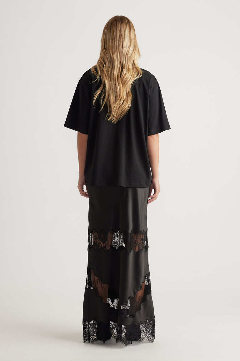 Back view of woman wearing a relaxed black oversized tee paired with a floor-length black lace-trimmed skirt