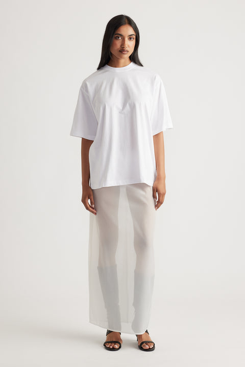 Woman wearing a relaxed white oversized tee paired with a sheer maxi skirt and black open-toe sandals for a modern look