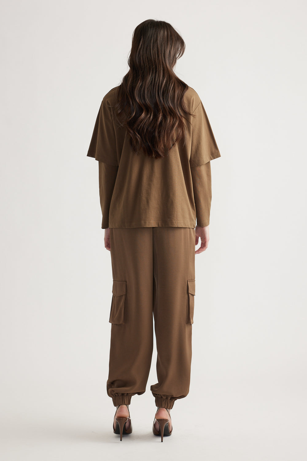 Back view of woman wearing relaxed brown cargo pants and a layered oversized brown tee with long sleeves underneath