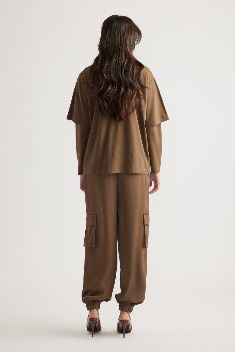 Back view of woman wearing relaxed brown cargo pants and a layered oversized brown tee with long sleeves underneath