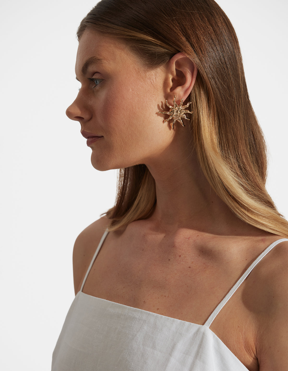 Portrait of woman wearing textured metal Tara Sun Earrings, gallery position 2, with neutral white top and natural lighting.
