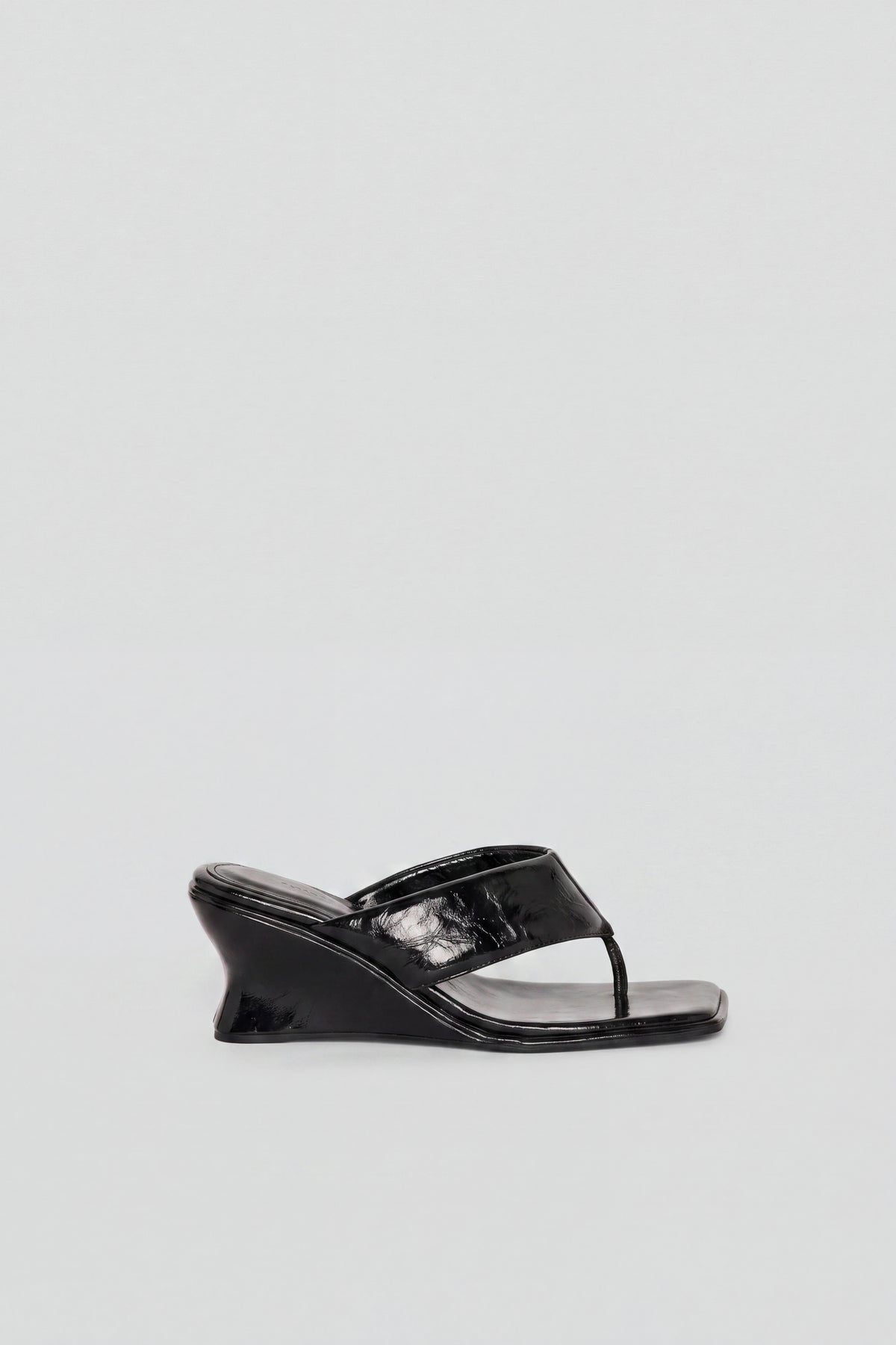 Side view of black glossy wedged thong heel sandal with sculptural heel and toe post detail