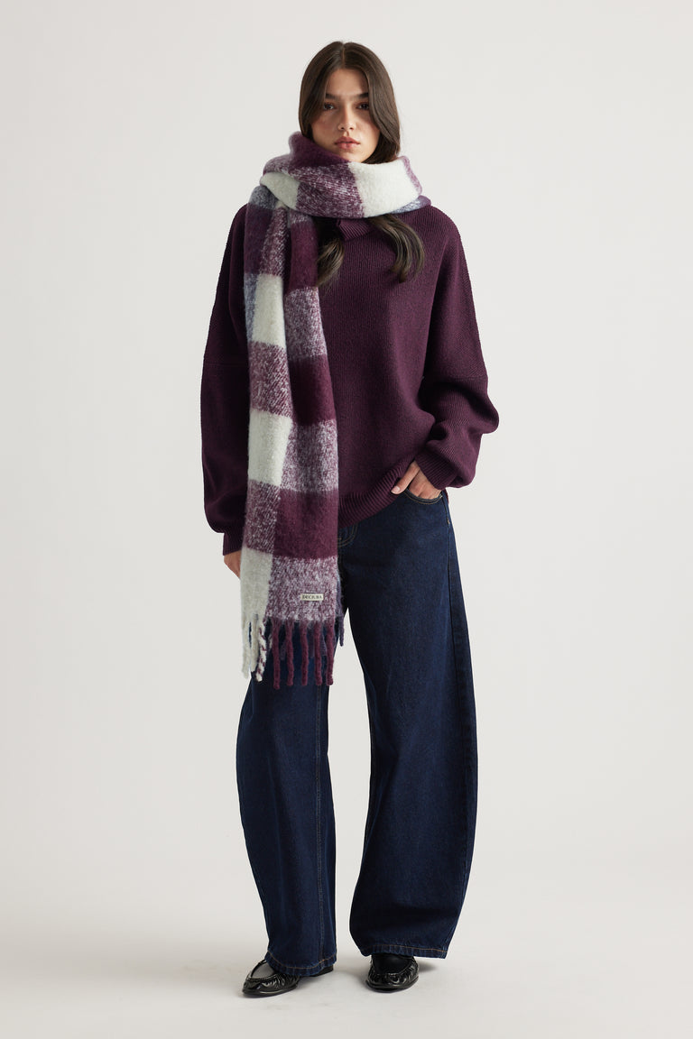 Woman wearing a cozy plum sweater with wide-leg dark jeans and a long checked scarf in soft burgundy and cream tones