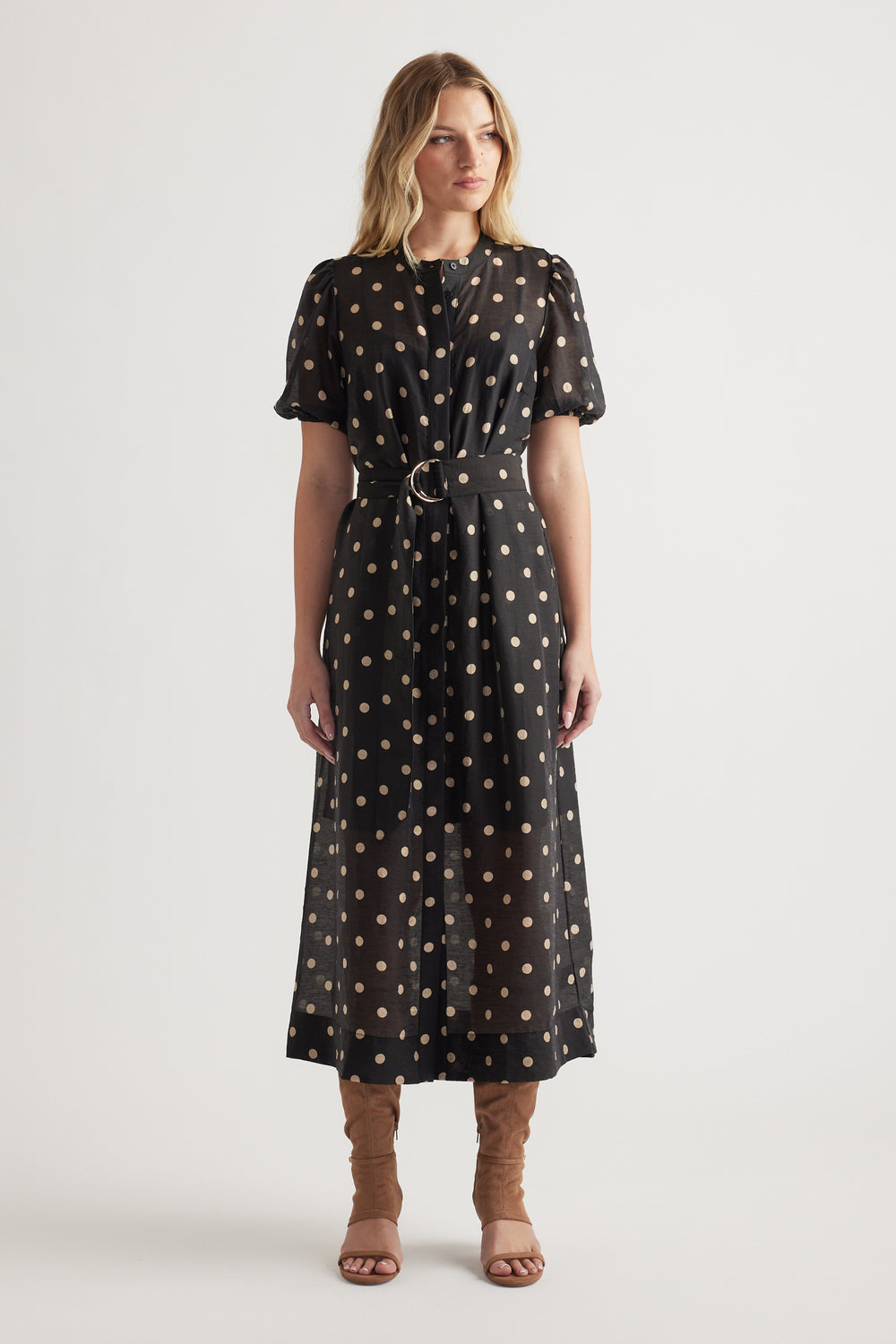 Woman wearing a black midi dress with beige polka dots, puff sleeves, cinched waist, and brown heeled sandals
