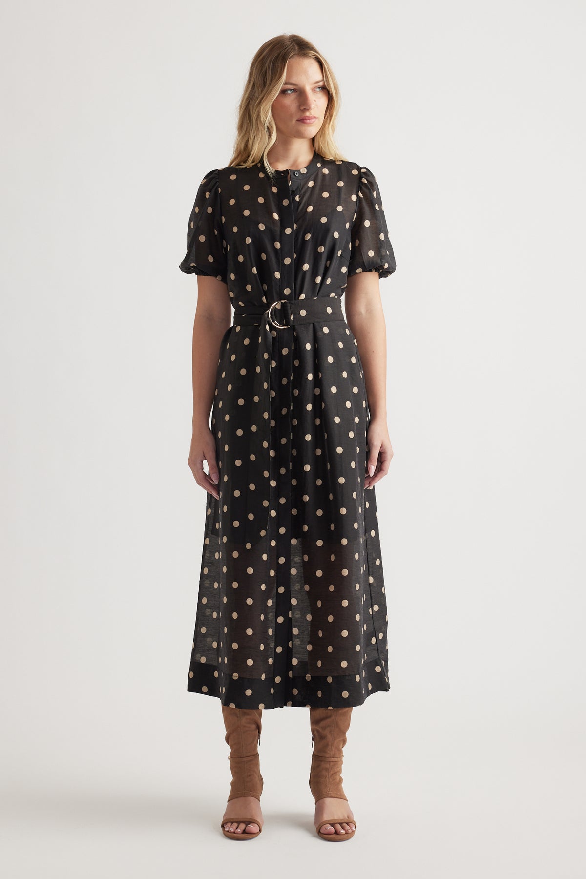 Woman wearing a black midi dress with beige polka dots, puff sleeves, cinched waist, and brown heeled sandals
