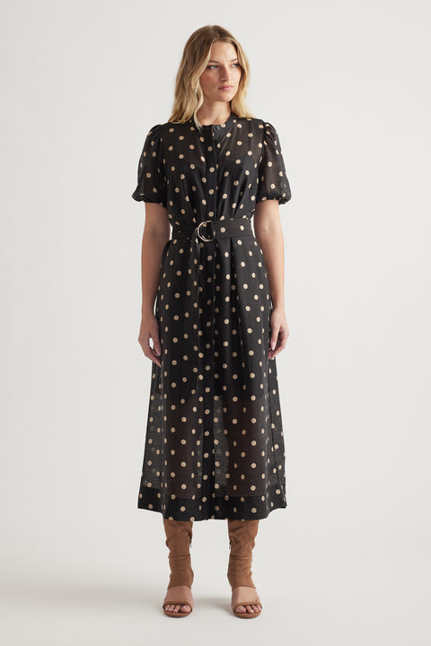 Woman wearing a black midi dress with beige polka dots, puff sleeves, cinched waist, and brown heeled sandals