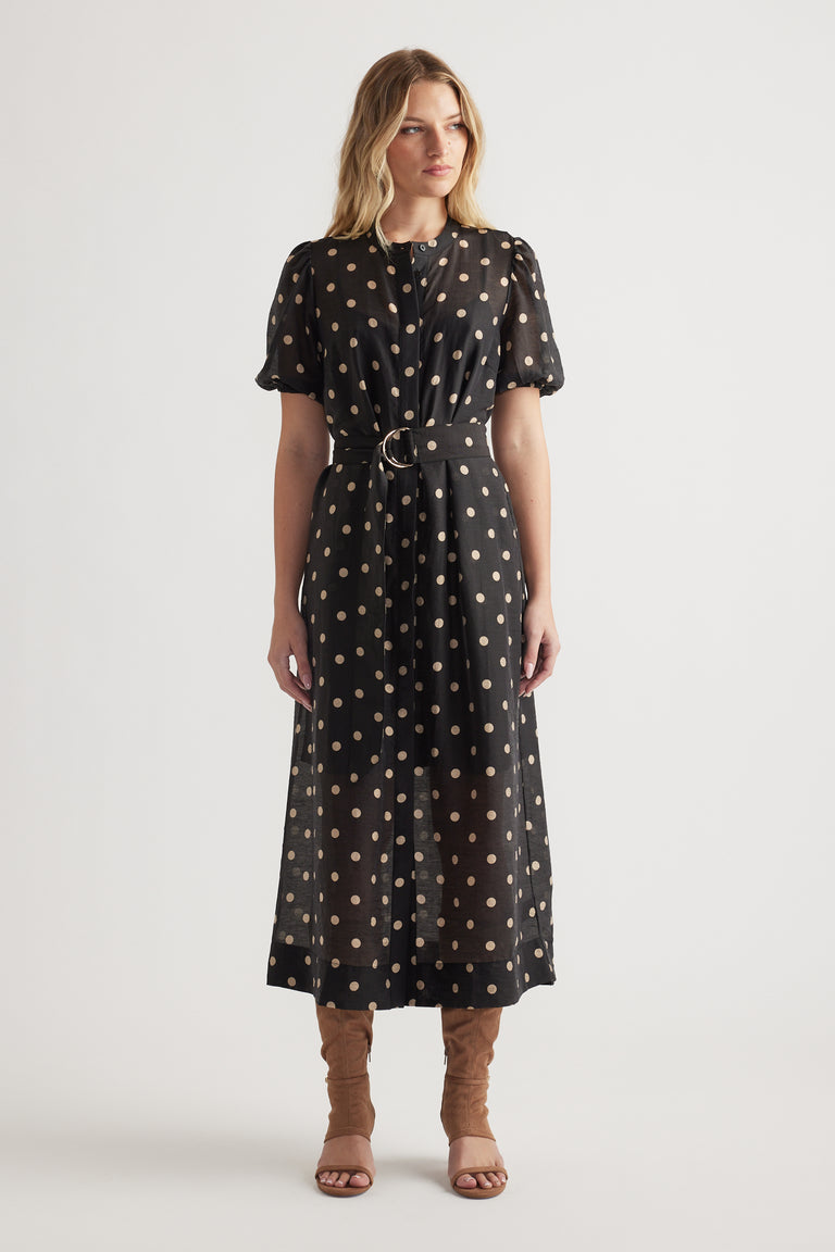 Woman wearing a black midi dress with beige polka dots, puff sleeves, cinched waist, and brown heeled sandals