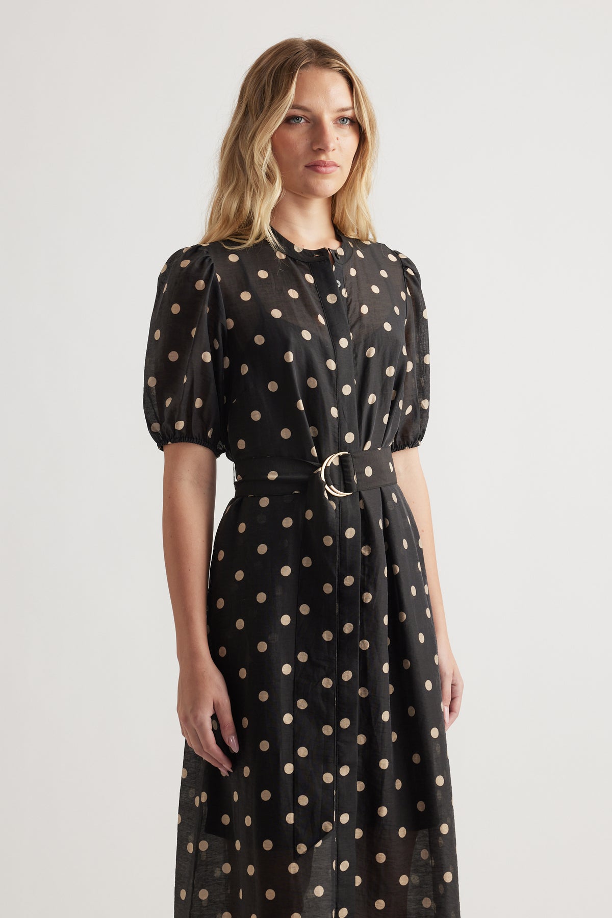 Woman wearing a black midi dress with puff sleeves, beige polka dots, and a belted waist for a chic, effortless look
