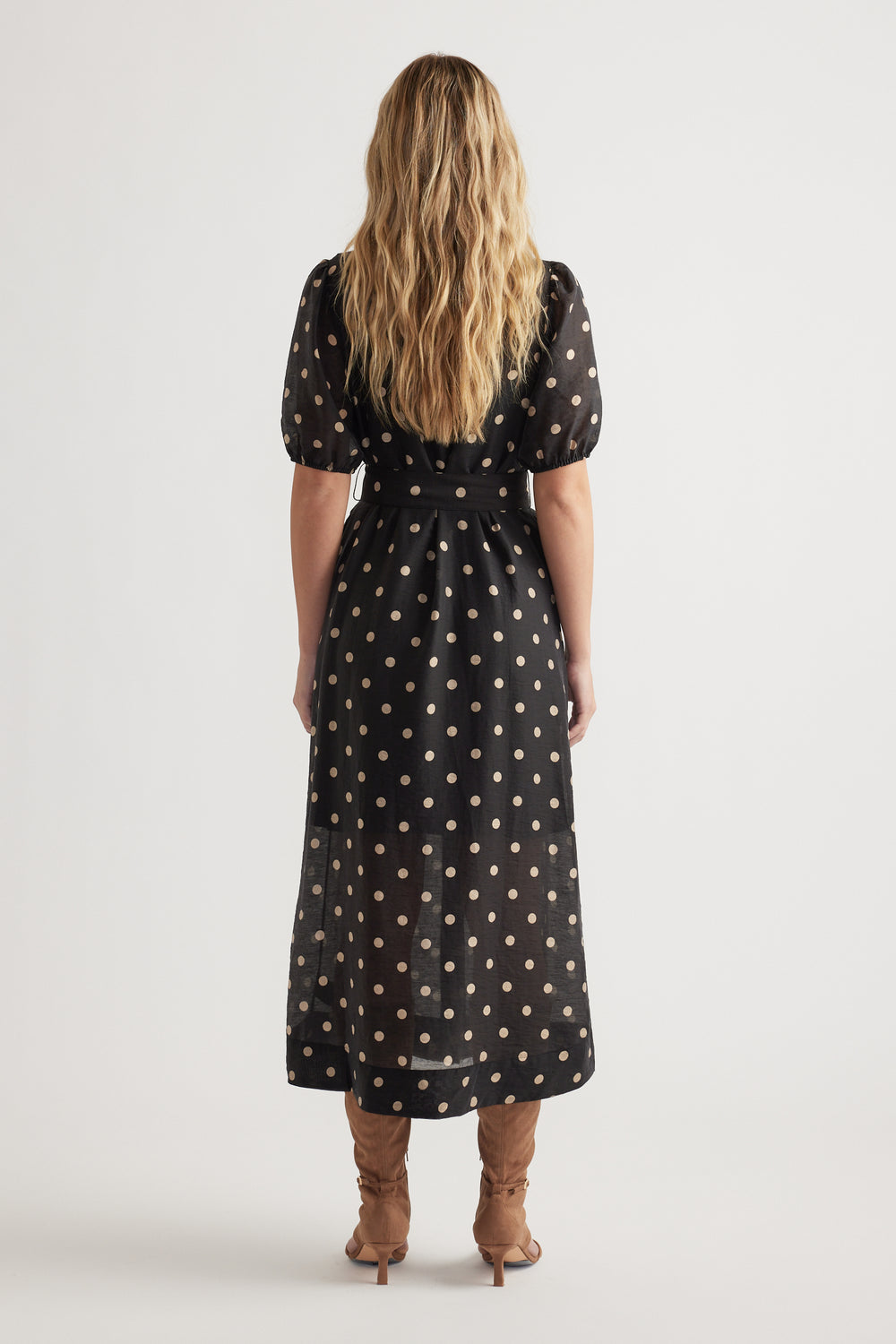 Back view of woman wearing a black midi dress with puff sleeves and beige polka dots paired with tan boots.