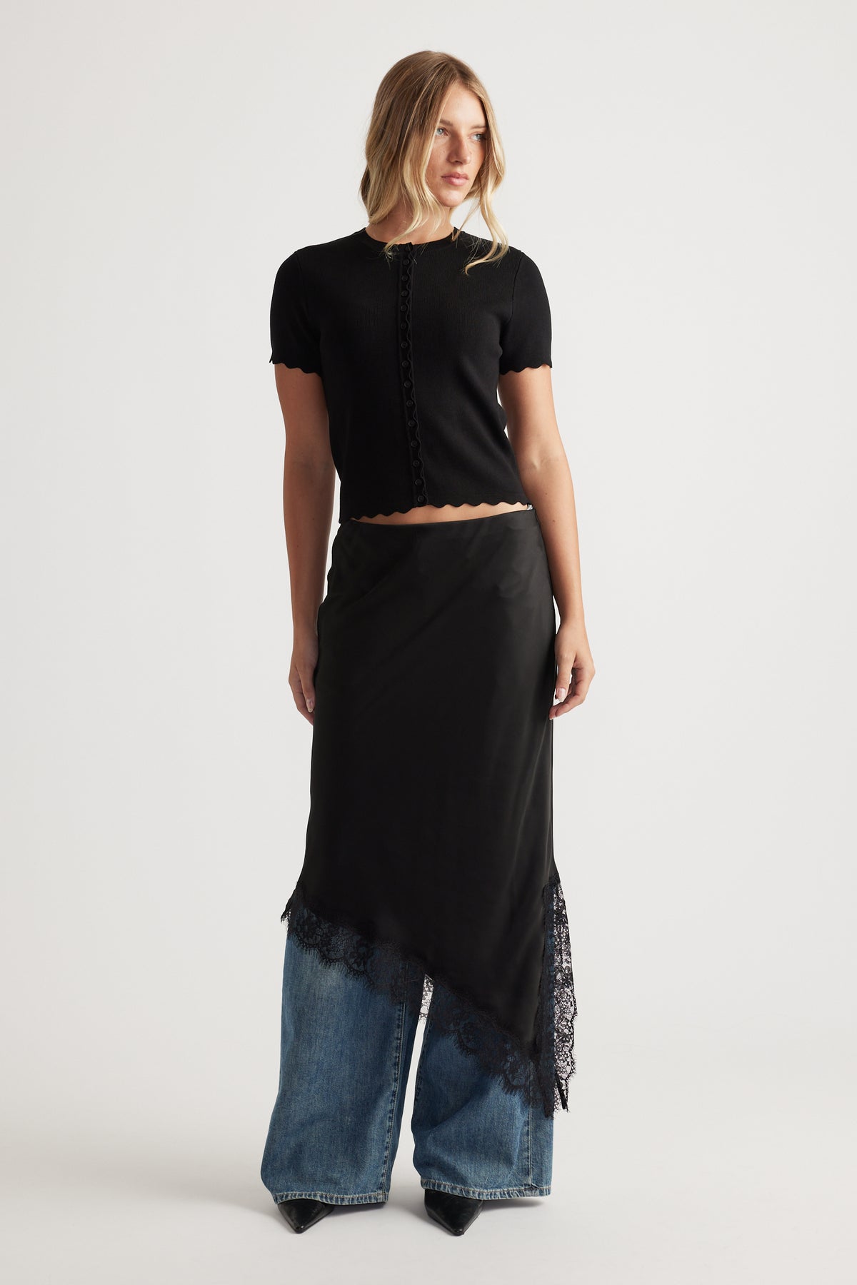 Woman wearing a black Maya Scallop Trim Button Top with short sleeves paired with wide-leg jeans and pointed black boots