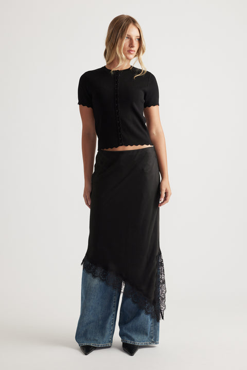 Woman wearing a black Maya Scallop Trim Button Top with short sleeves paired with wide-leg jeans and pointed black boots