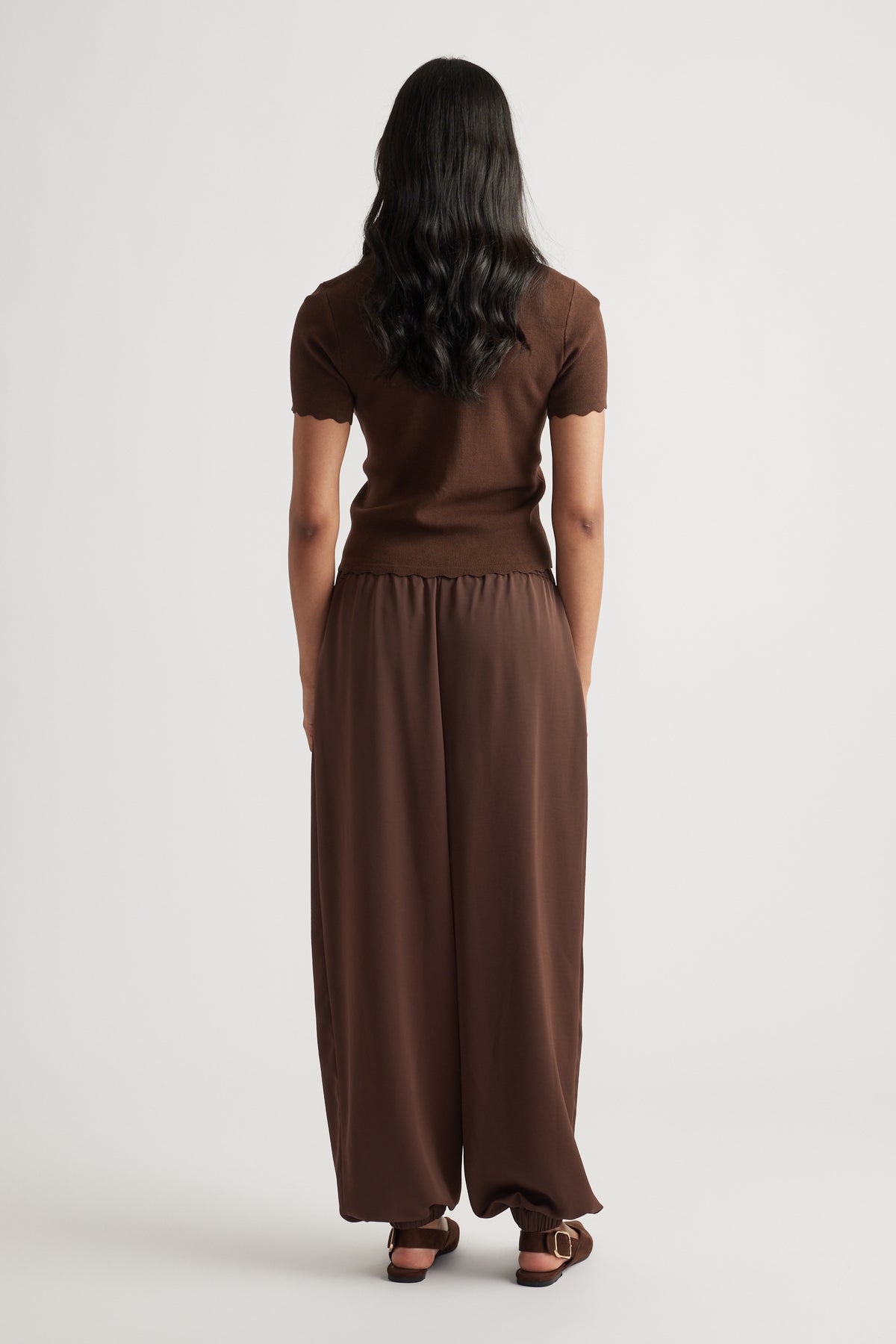 Back view of Maya Scallop Trim Button Top in warm brown with short scalloped sleeves, paired with relaxed brown pants.