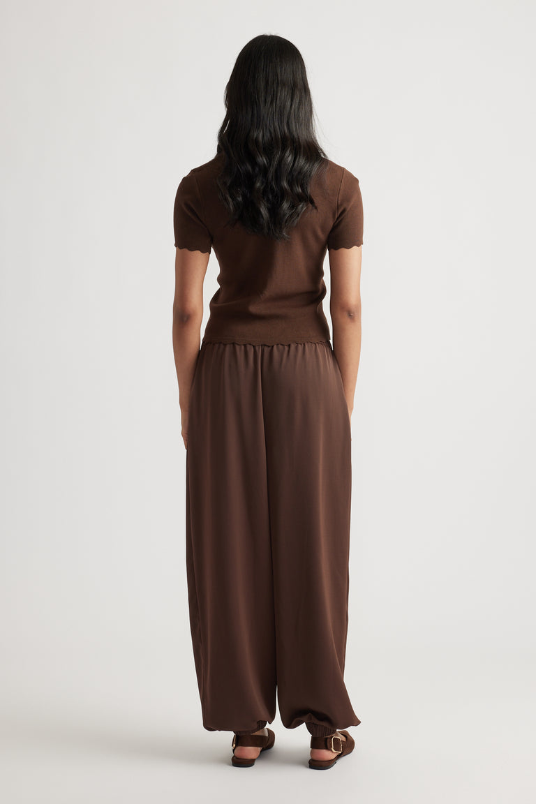 Back view of Maya Scallop Trim Button Top in warm brown with short scalloped sleeves, paired with relaxed brown pants.