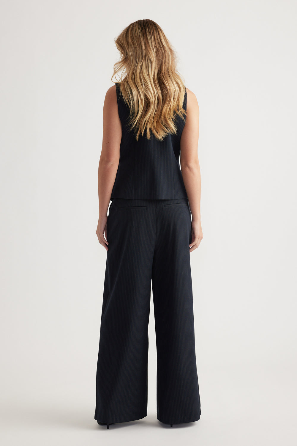Woman seen from behind wearing a black ribbed side tie vest paired with wide-leg coordinating pants against a plain background